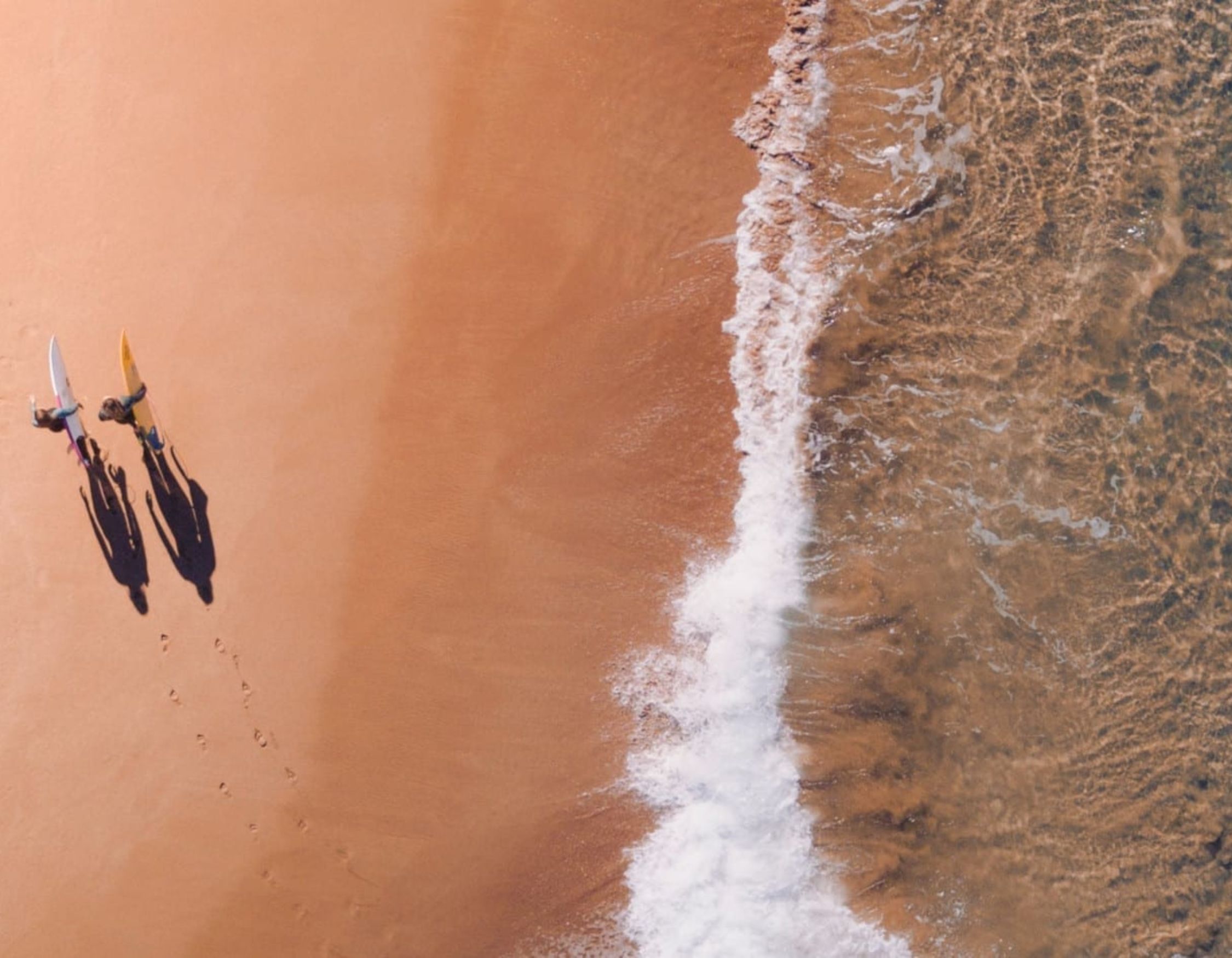 Two surfers running into the water at Bondi Beach, Sydney, at golden hour